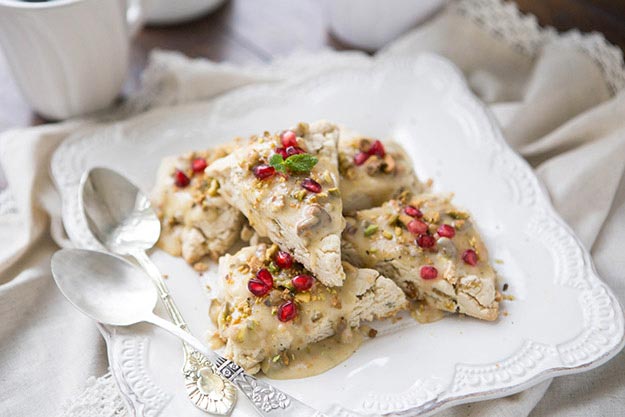 Honey pistachio scones garnished with pomegranate seeds and drizzled with honey on an ornate white plate.