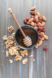 Honey with dipper in a bowl with mixed nuts and walnuts on a wooden background.