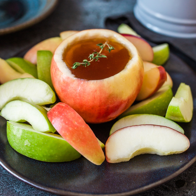 Apple filled with honey, surrounded by apple slices on a dark plate, a creative and healthy snack presentation.