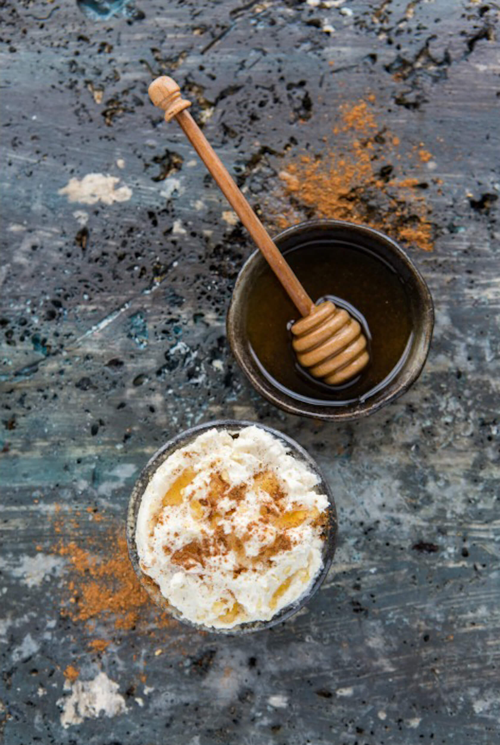 Soft, whipped butter with cinnamon beside honey with dipper in a bowl on a distressed surface.