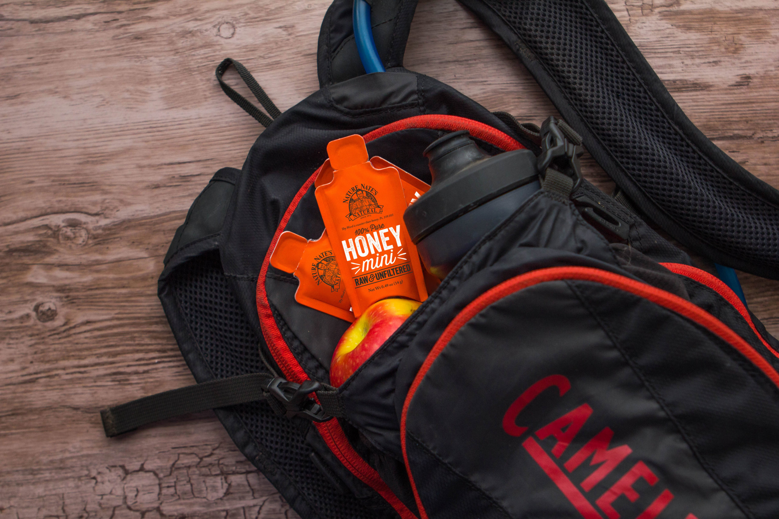 Backpack with Nate's honey minis and water bottle on a wooden floor.