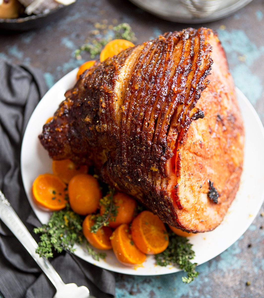 Honey-glazed ham on a platter with citrus slices and parsley with a patterned napkin.