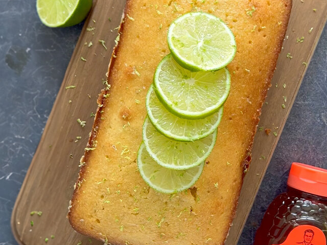 Rectangle honey lime cake loaf topped with lime slices and lime zest. Displayed next to Nate's honey bottle.