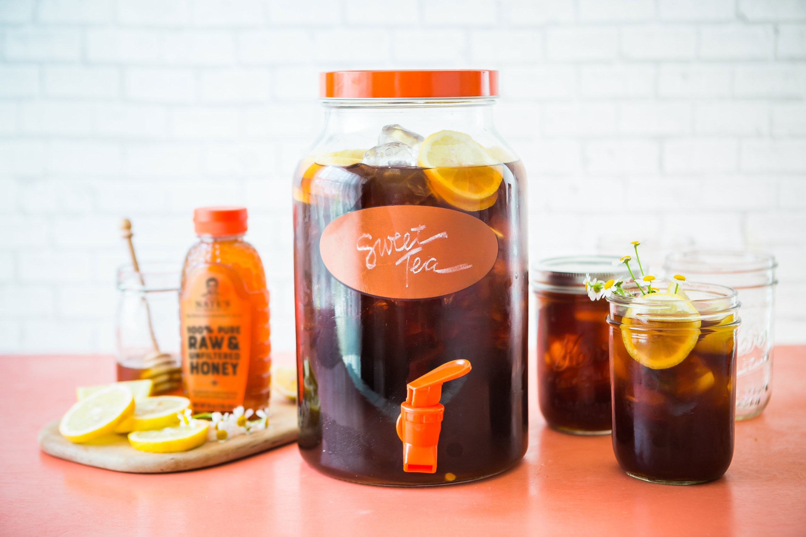 A bright setup featuring a large jar of sweet tea, smaller servings, lemon slices, and a bottle of Nate's honey.
