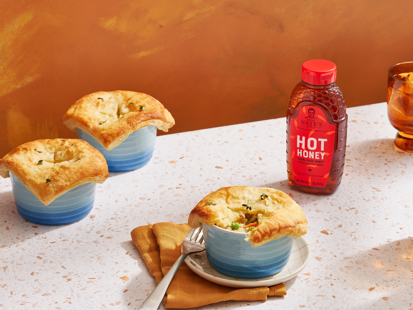 Hot honey chicken pot pies in blue ramekins with a bottle of Nate’s hot honey.