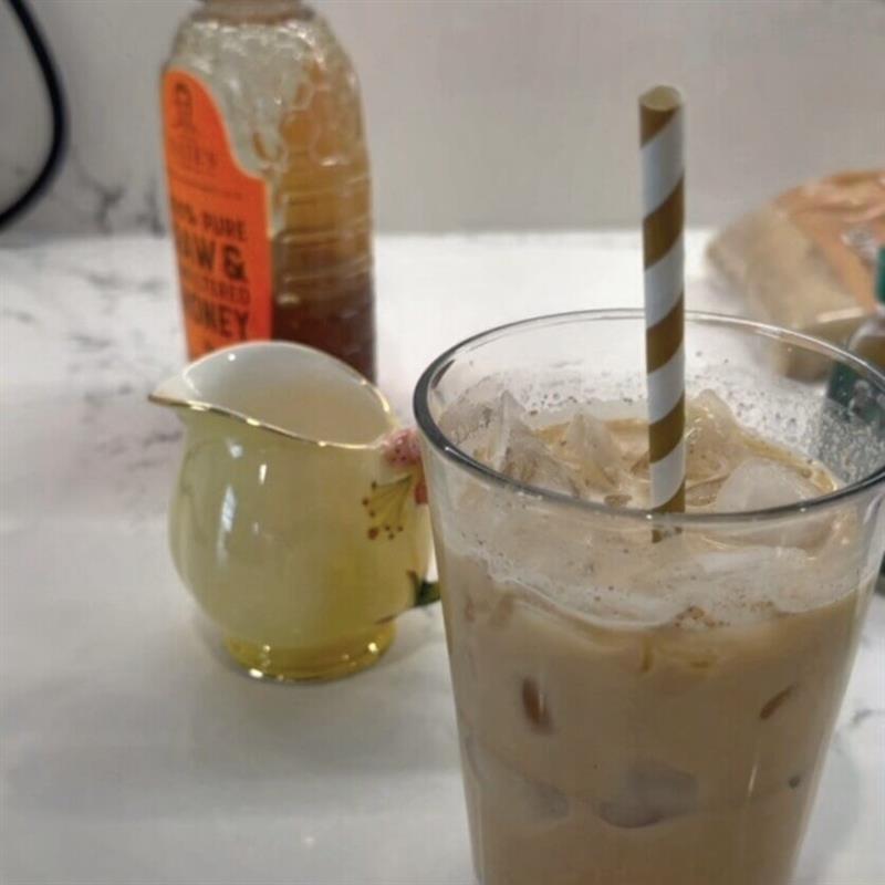 Teddy Graham Latte in clear glass cup with a Nate's honey in the background.