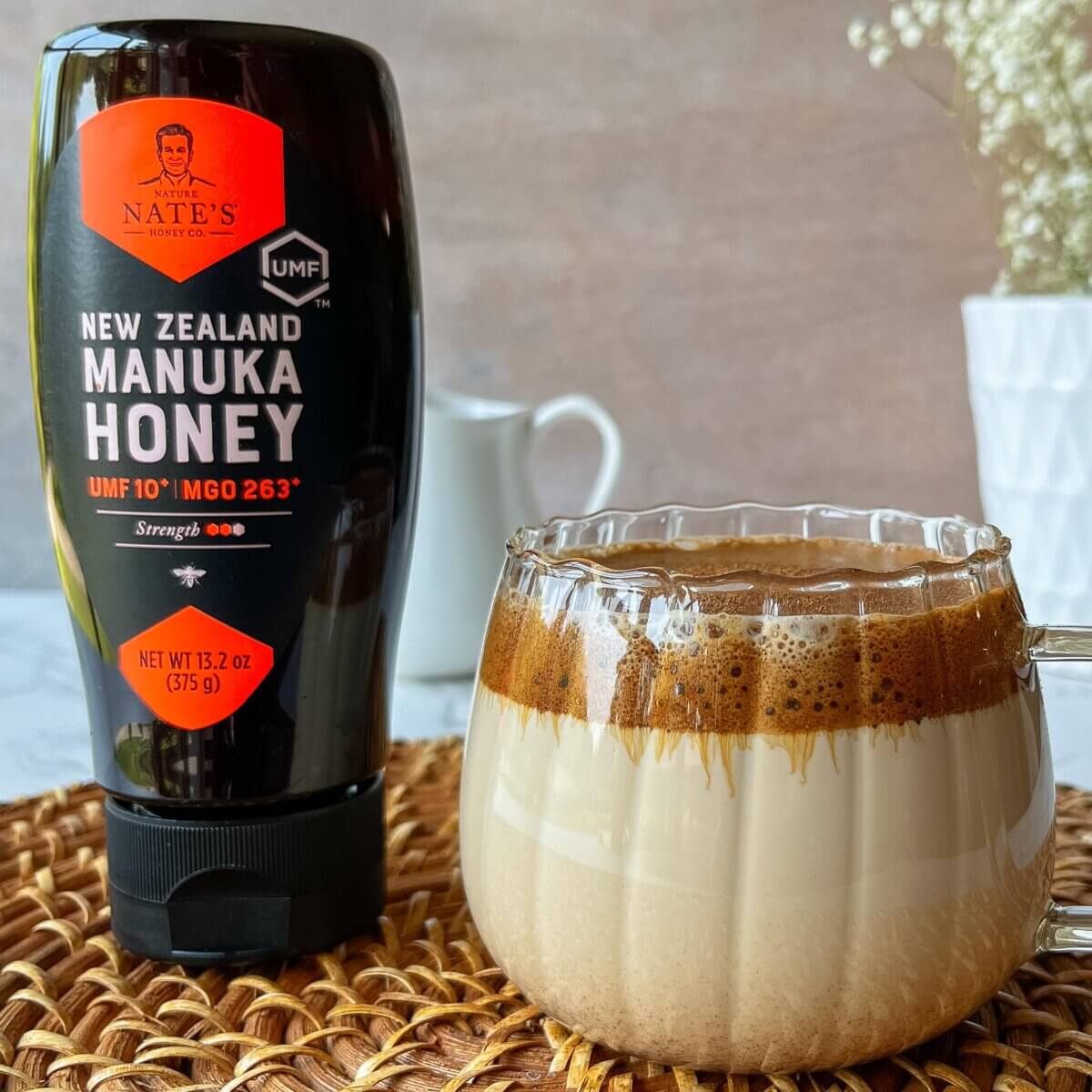 Clear pumpkin shaped mug filled with a pumpkin spice latte displayed next to Nate's Manuka Honey.