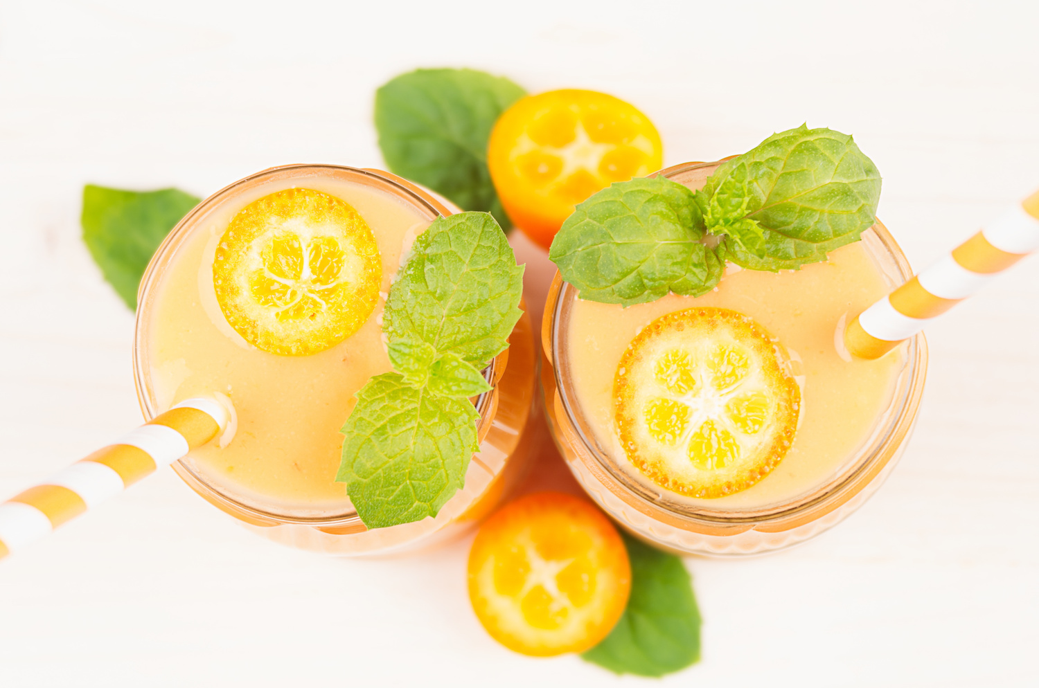 Two glasses of citrusy orange beverage garnished with mint leaves and kumquat, showcasing a refreshing summer drink.