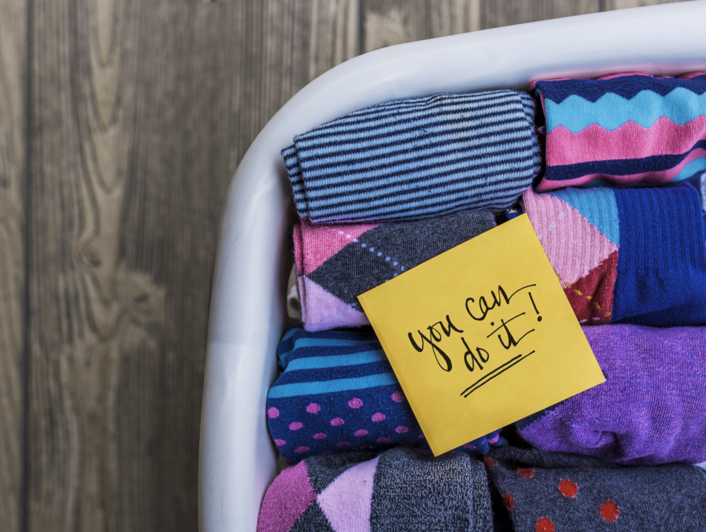 Folded colorful socks in a laundry basket with an encouraging note.