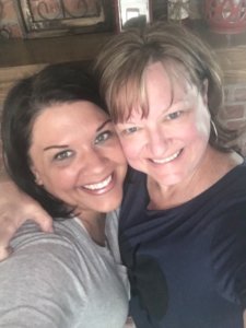 A close-up selfie of two smiling women, sharing a warm, friendly moment together.