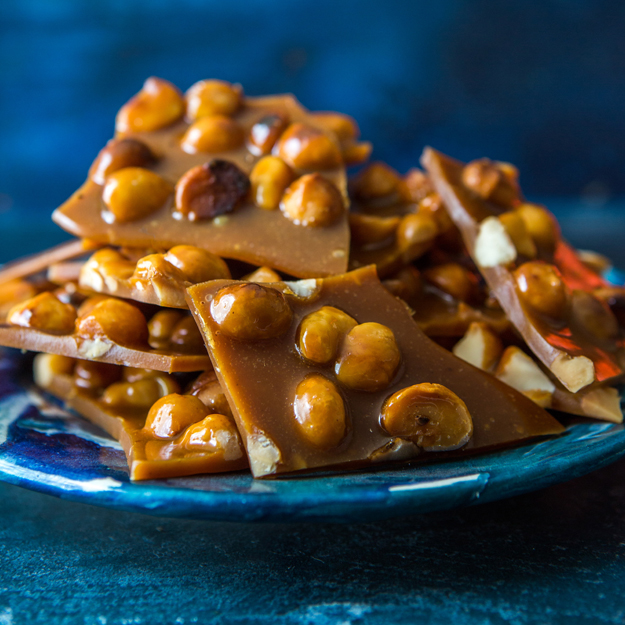 Stacked macadamia honey brittle pieces on blue ceramic plate, dark moody lighting.