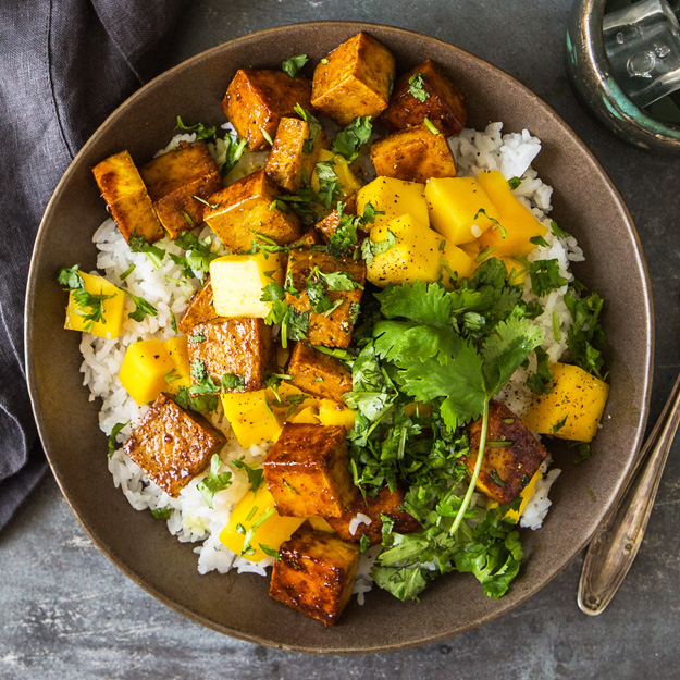 Tofu mango bowl with rice, cilantro atop, rustic bowl, dark textured backdrop.
