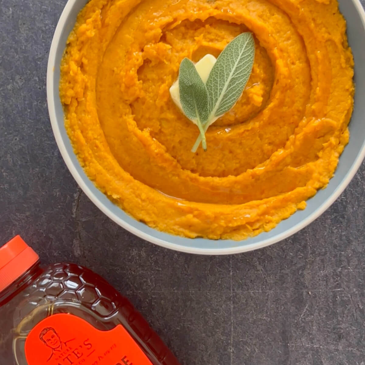 Bowl filled with mashed sweet potatoes and garnished with a sage leaf.