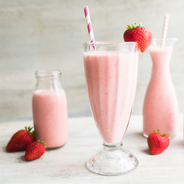 Strawberry milkshakes in glasses with fresh strawberries, light background.