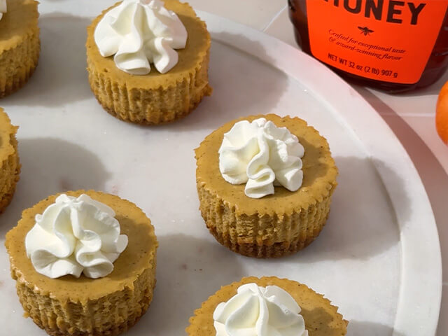 Round petite pumpkin cheesecake treats topped with whipped cream plated on white plate.