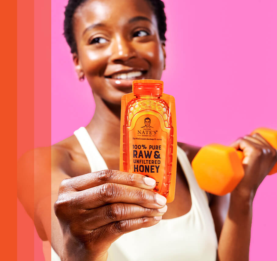 Woman holding Nate's honey mini in one hand and an orange dumbbell in the other hand.