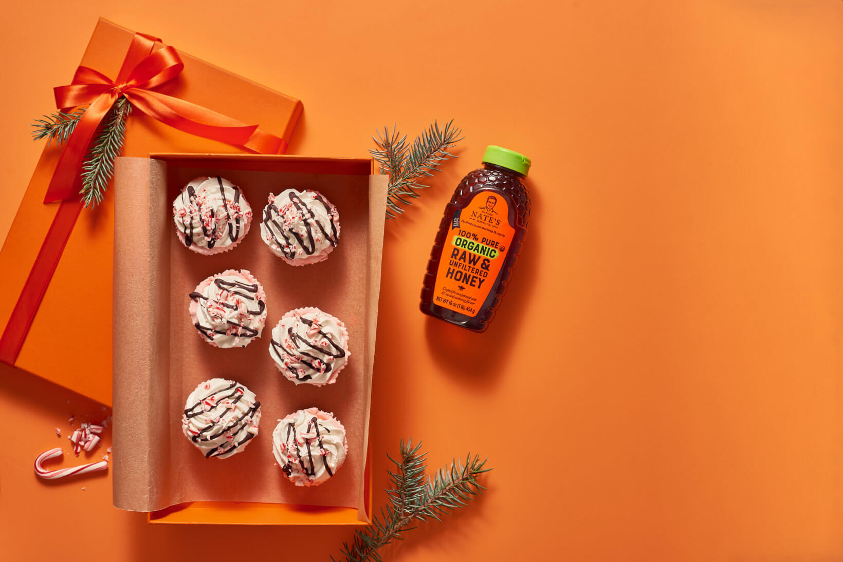 Mini peppermint pies in a gift box with a bottle of Nate’s organic honey on an orange background with holiday decor.