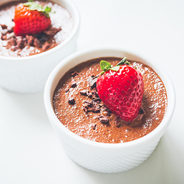 Chocolate mousse in white bowls with strawberry topping and chocolate nibs, on a neutral backdrop.