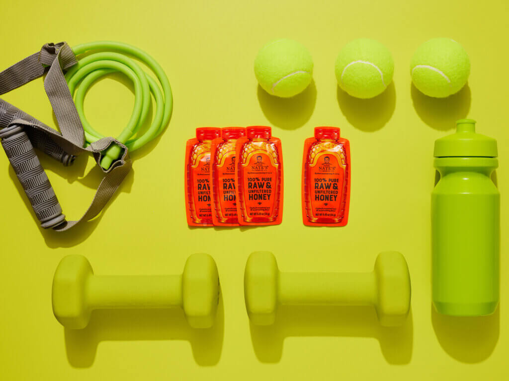 Nate’s honey minis centered on a neon yellow background with neon yellow workout equipment, tennis balls and water bottle.