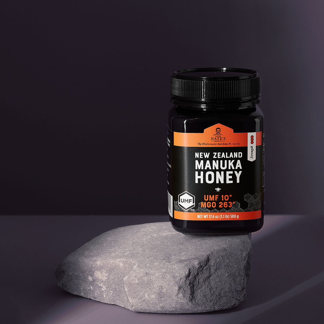 A jar of Nate’s New Zealand manuka honey UMF 10+ on a rock, with a purple-grey background.