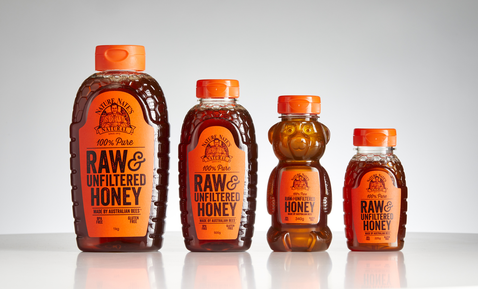 Four bottles of Nate's raw & unfiltered honey in different sizes on a reflective surface.