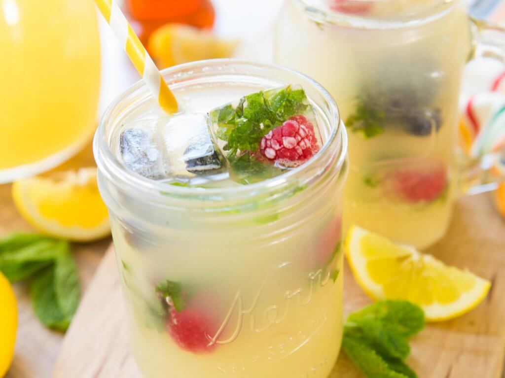 Mason jars filled with refreshing lemonade, garnished with mint leaves and raspberries, ready for a summer sip.