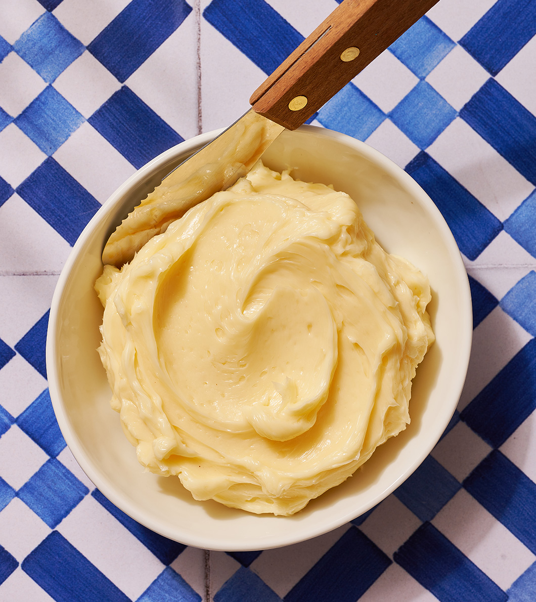 bowl of honey butter with butter knife on blue and white tile background