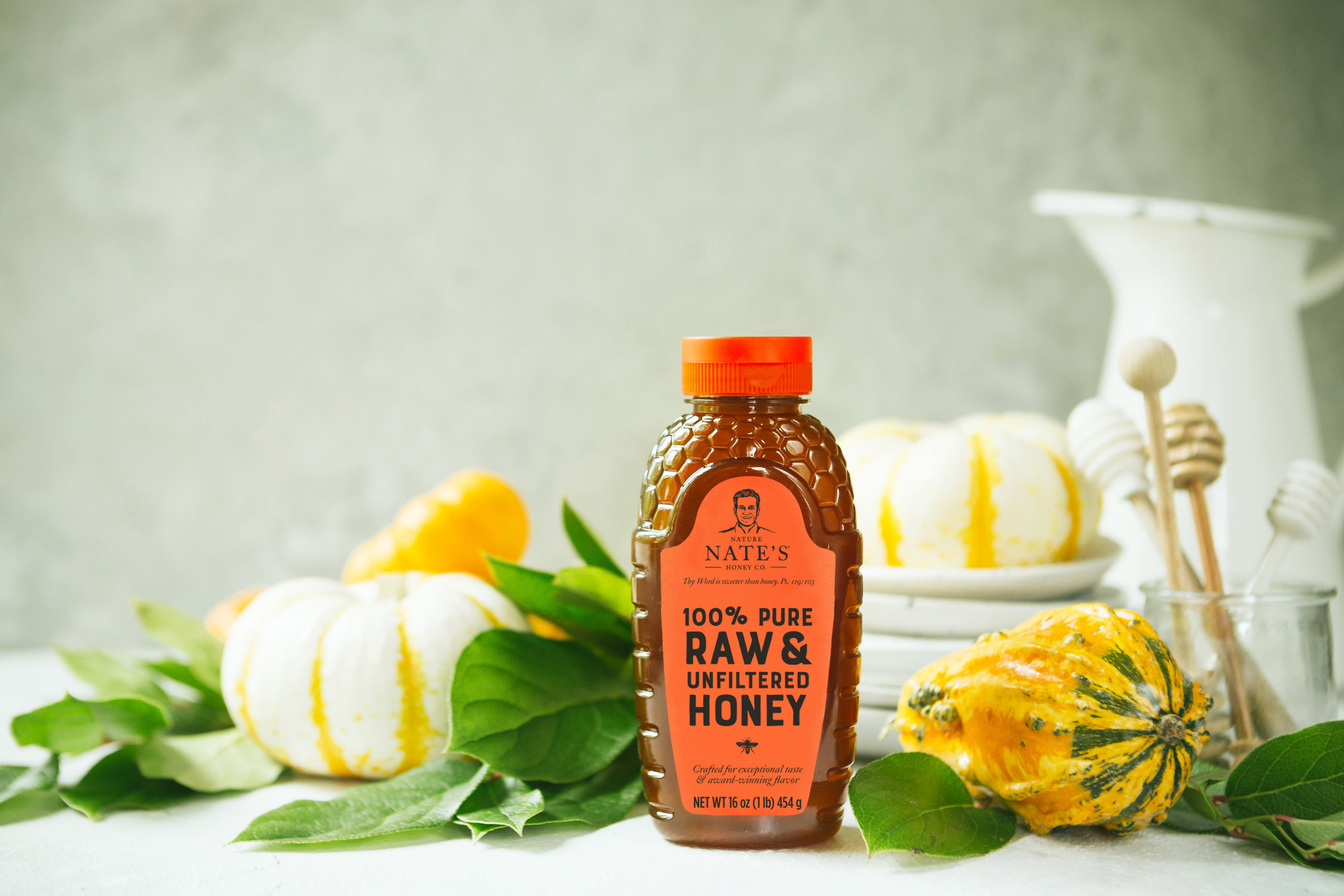 Nate's honey bottle on a table with decorative pumpkins and green leaves, hinting at autumn vibes.
