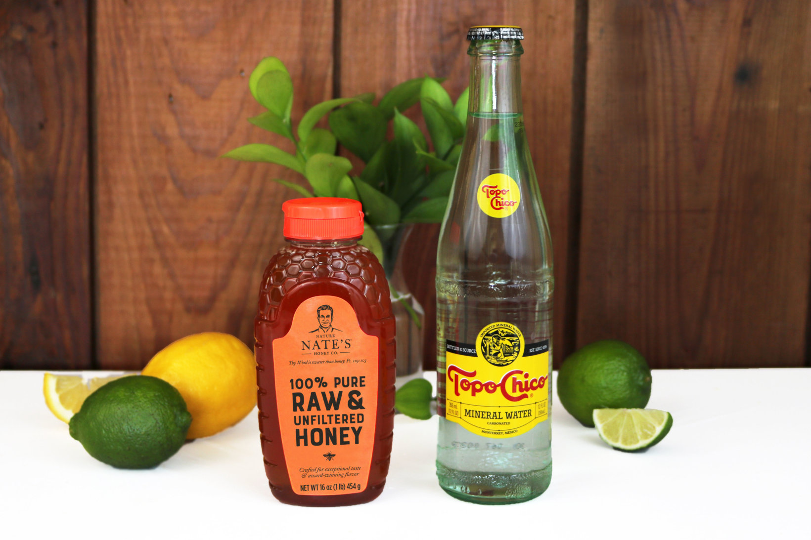 Nate's honey bottle with citrus fruits and mineral water on wooden backdrop.