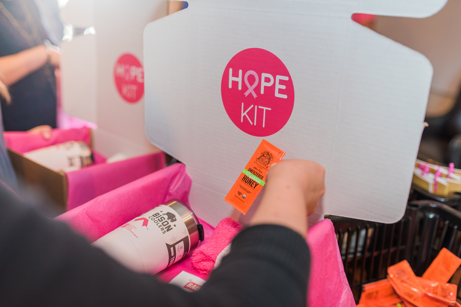 A person assembles a HOPE KIT, with pink tissue paper and a Nate's honey packet inside.