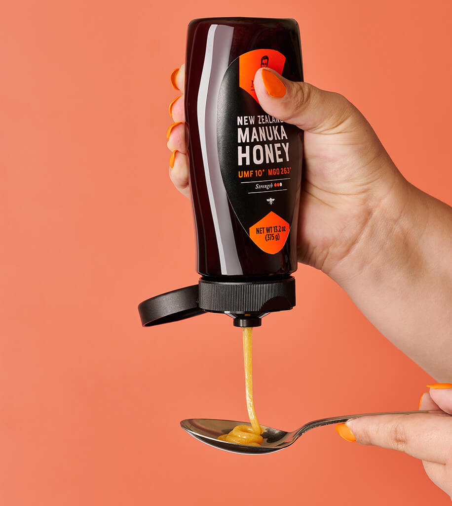 A tube and jar of New Zealand Manuka honey with UMF 10+ and UMF 7+ ratings,  on a stone against a brown background.