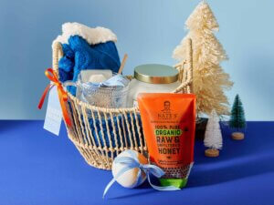 A blue- and white-themed gift basket with a Nate’s organic honey pouch and festive decorations on a blue surface.