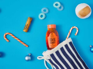 Nate’s honey bottle with festive candy canes, ornaments and a striped stocking on a blue background.