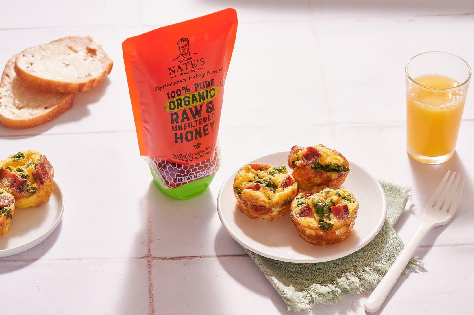 On a sunlit table, egg bites rest on a plate beside a pouch of Nate’s organic honey with toast and orange juice nearby.
