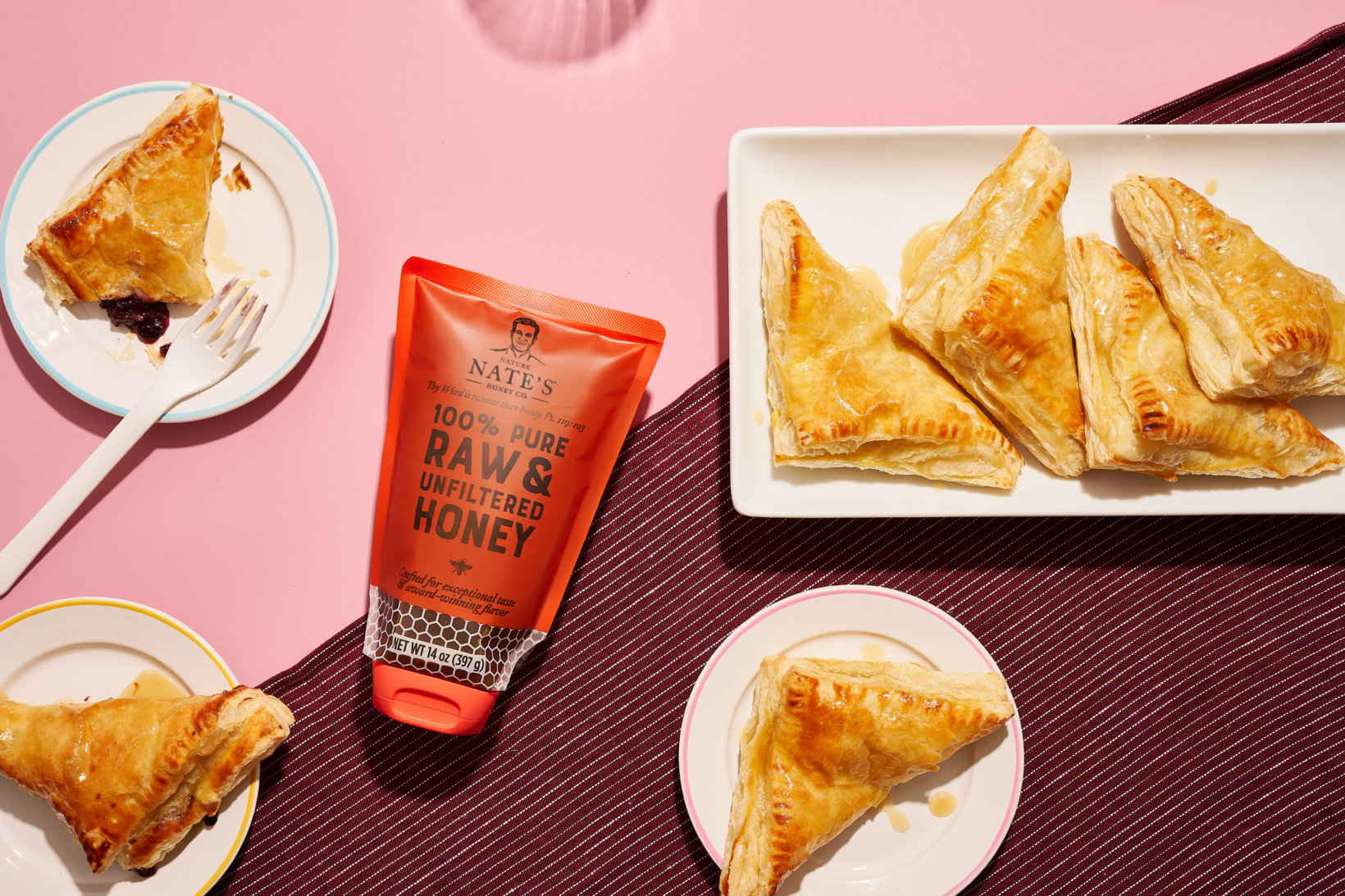 Turnovers on a plate, a pouch of Nate's honey and turnovers on smaller plates, all on a pink surface. 