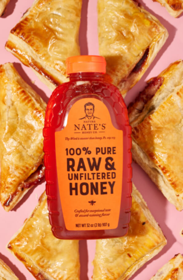 Bottle of Nate's honey with cherry turnovers on a pink backdrop.