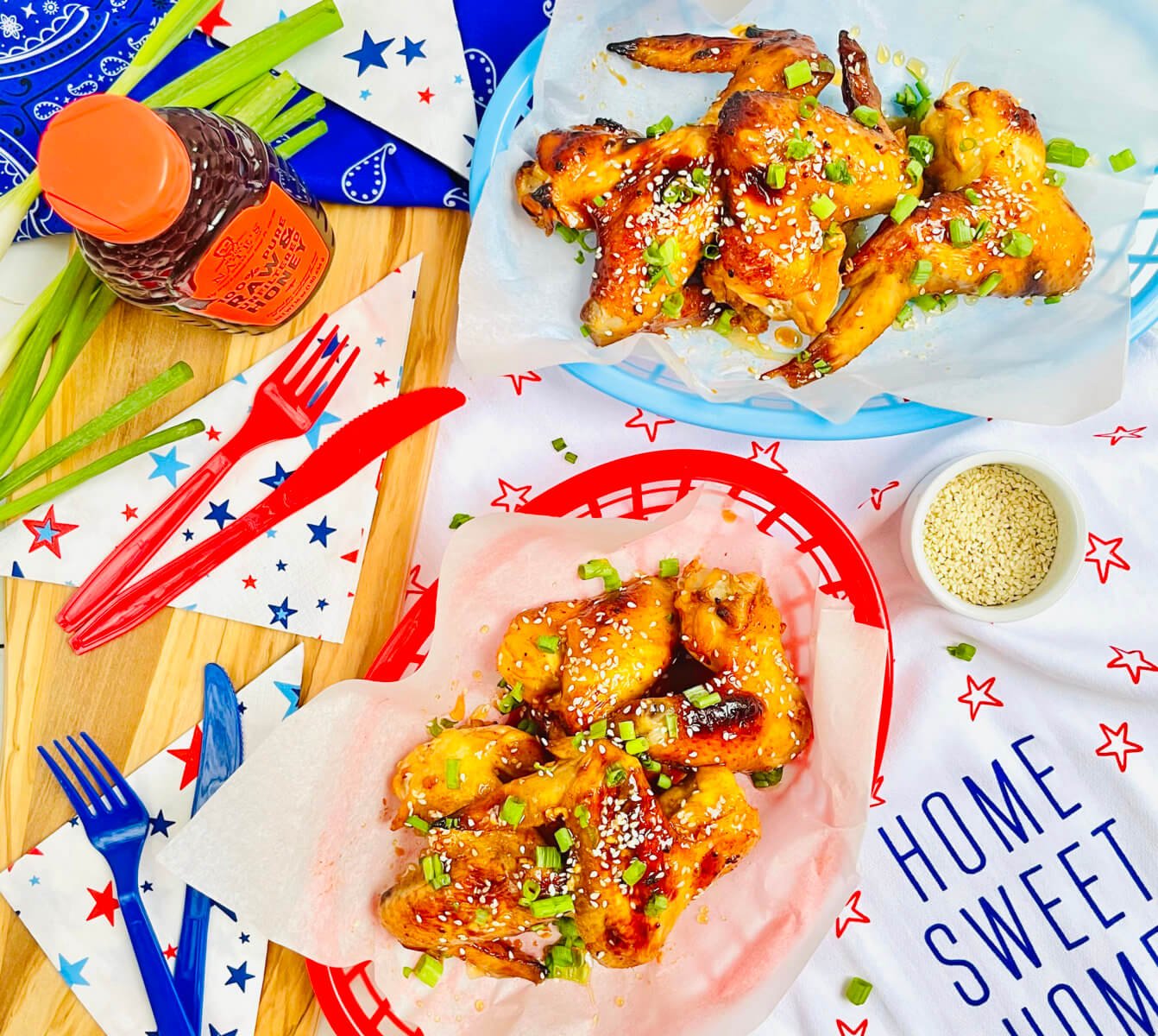 Honey-glazed Korean chicken wings on patriotic tableware with a bottle of Nate’s honey and festive decorations.