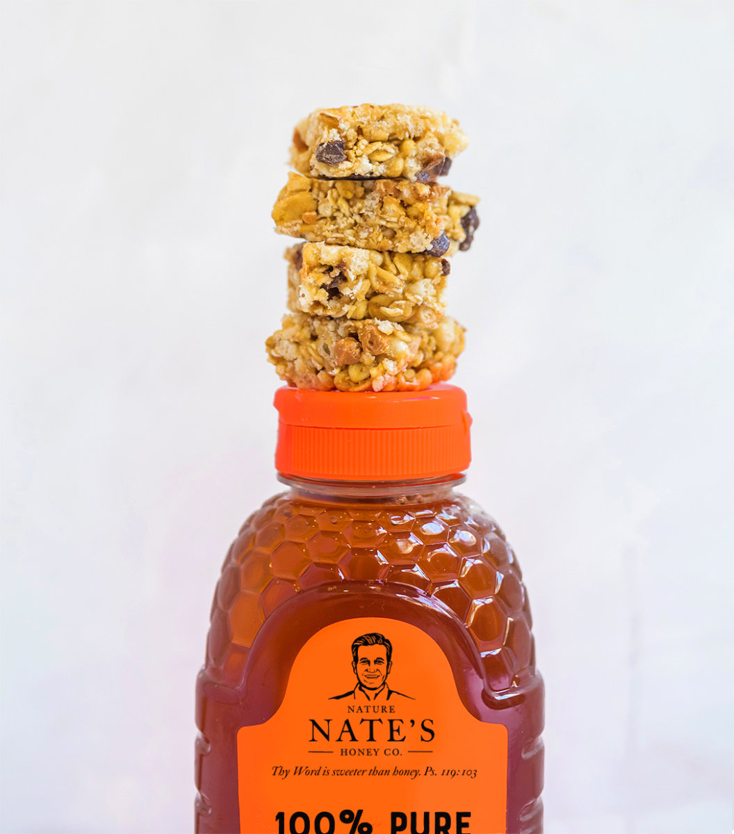 Granola bars stacked on top of a bottle of Nate's honey against a white background.