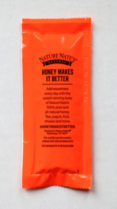 A vibrant orange honey packet from Nature Nate’s with text about its purity and uses, set against a white backdrop.