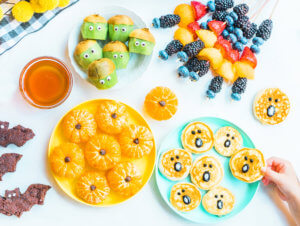 Kids’ snacks with kiwi, berries, oranges, pancakes and brownies, arranged on vibrant plates next to a bowl of honey.