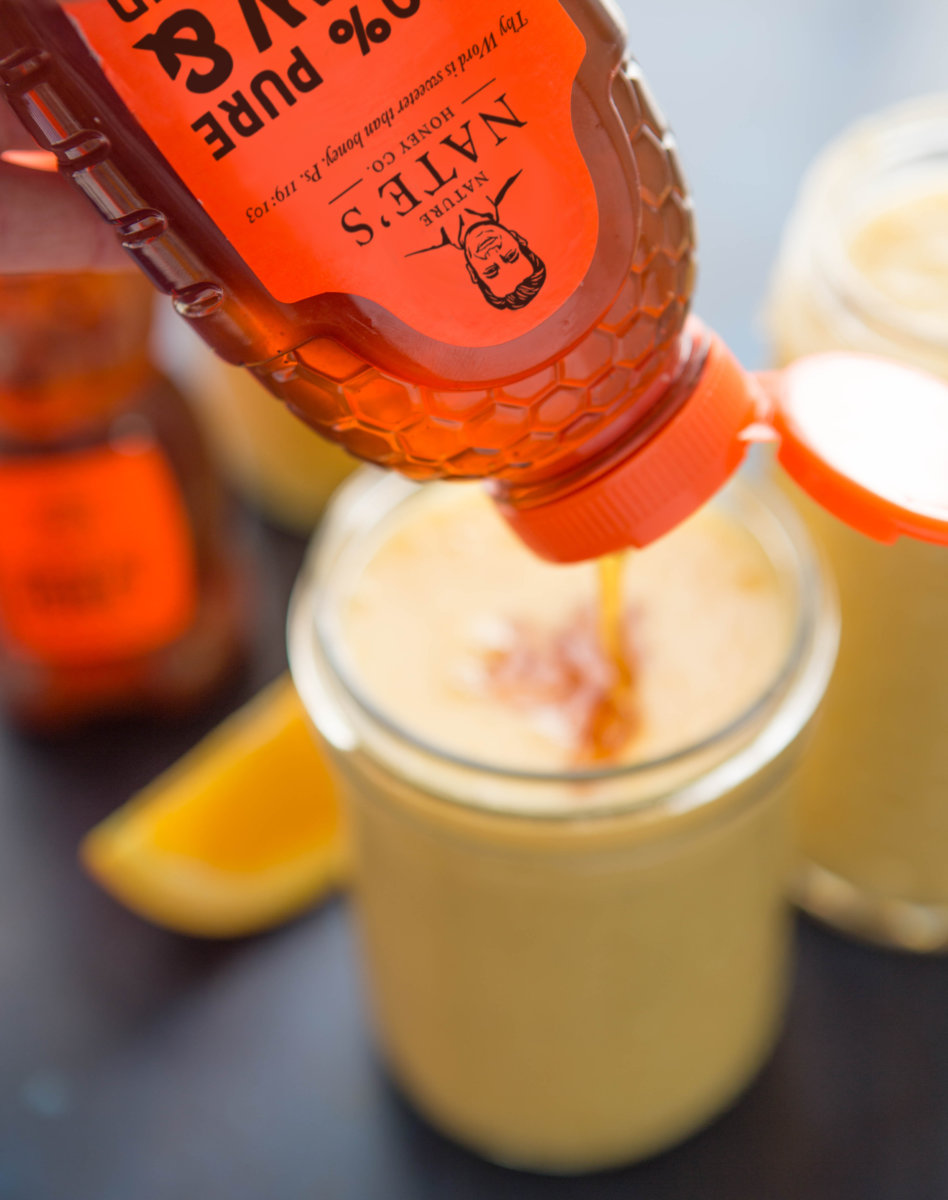 Nate's honey being poured into a jar with a beverage on a dark surface.