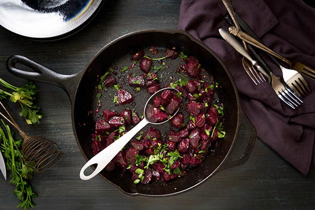 Roasted beets in a cast iron skillet with herbs, dark linen napkin, rustic setting.