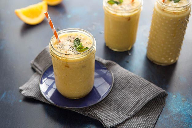 Orange, pineapple and mango smoothies with mint on a blue plate and dark linen, dark blue surface.