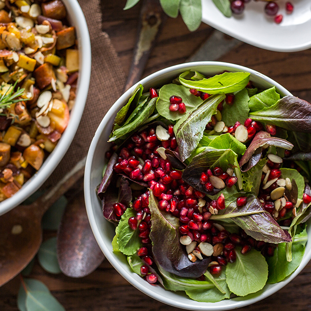 Fresh salad with mixed greens, pomegranate seeds and almonds in a white bowl, wooden background.