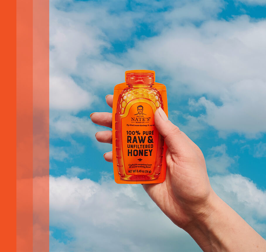 Hand holding Nate's honey mini with a cloudy sky in the background.