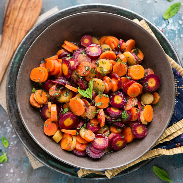 Herb-garnished carrot salad in a rustic bowl, on a dark stone surface with a napkin.