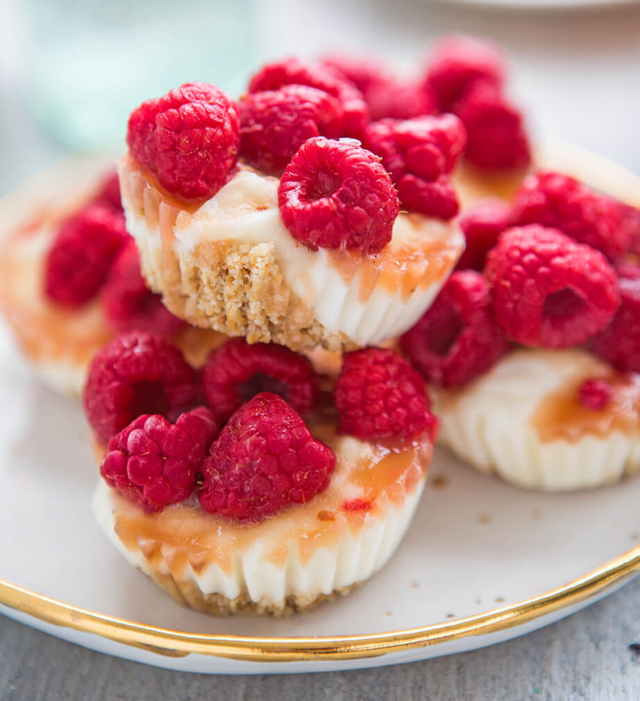 Mini cheesecakes topped with fresh raspberries and drizzled with honey, presented on a gold-rimmed plate.