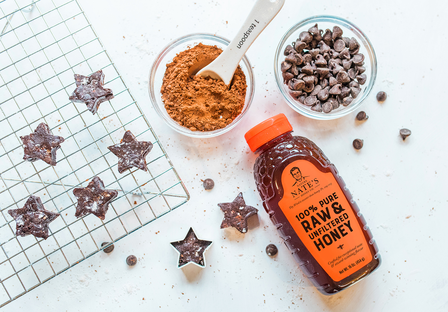 A bottle of Nate's honey with baking ingredients and star-shaped fudge on a light countertop.