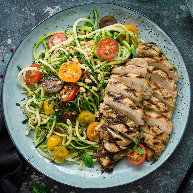 Grilled chicken slices with zucchini noodles and cherry tomatoes on a speckled plate.