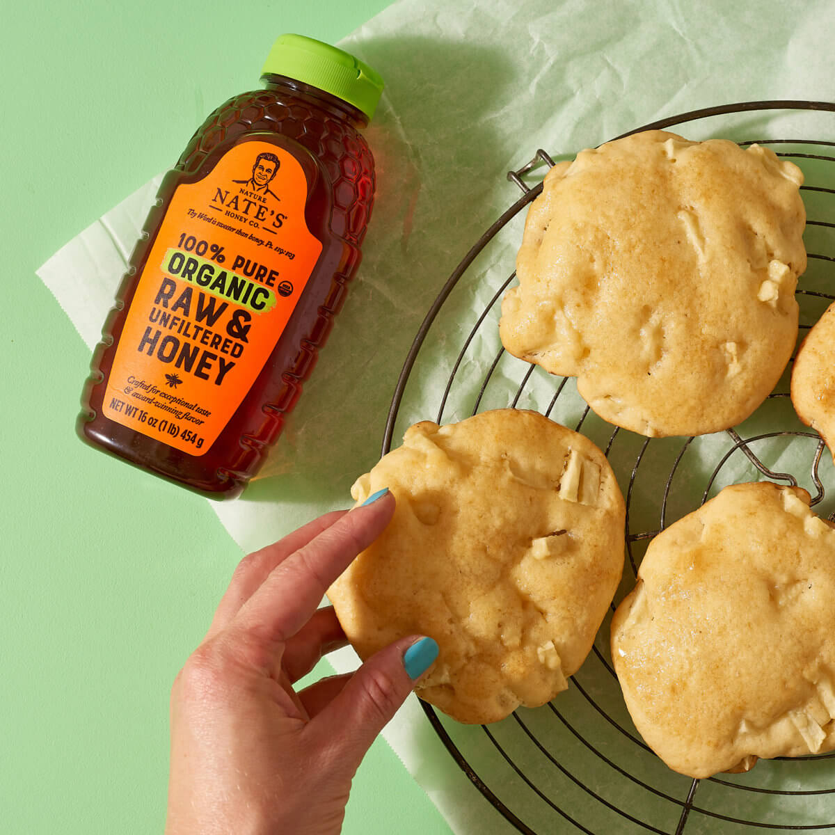 hand grabbing cookies on cooling rack next to bottle of Nate's Organic Honey on green background
